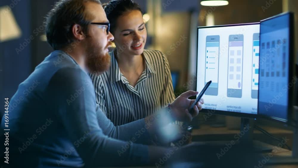 Handsome Male and Beautiful Female Mobile Application Designers Test and Discuss New App Features. They Work on a Personal Computer with Two Displays, in a Creative Office Space.