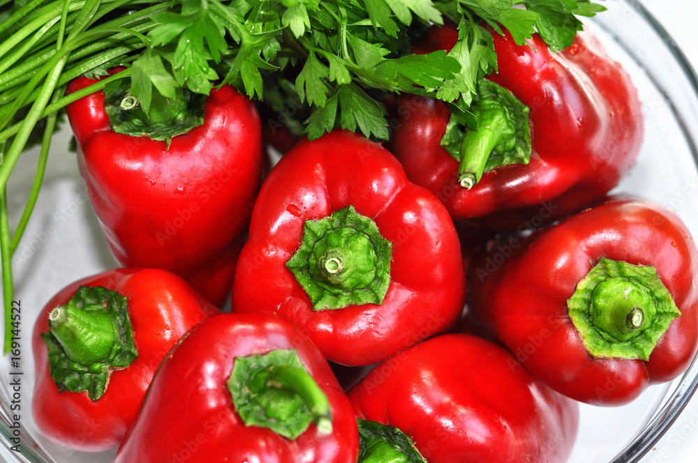Raw red organic peppers with bunch of aromatic green spice parsley in a glass bowl ready to cook with isolated on white Raw red organic peppers with bunch of aromatic green spice parsley in a glass bowl ready to cook with isolated on white