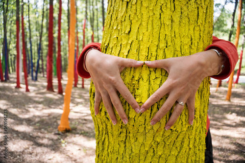Woman embrassing a colourful tree with shape of heart from hand, forest with painted trees as a protest against cutting trees. photo