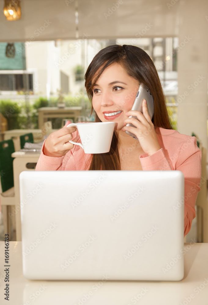 Close up of a young beautiful businesswoman working and drinking coffe while she is using her cellphone to make a call. Business concept Close up of a young beautiful businesswoman working and drinking coffe while she is using her cellphone to make a call. Business concept