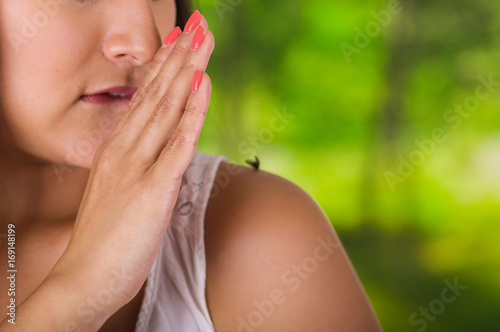Close up of a young woman using her hand to kill a mosquito over her shoulder  in a blurred green background