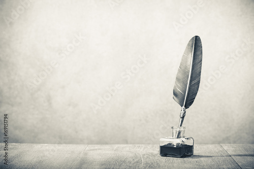 Quill pen with inkwell  on wooden desk. Vintage old style sepia photography