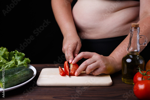 Dieting, healthy food, weight losing, well-being. Overweight fat woman slicing a tomato for salad. Organic tasty fresh low-calorie food, cooking process