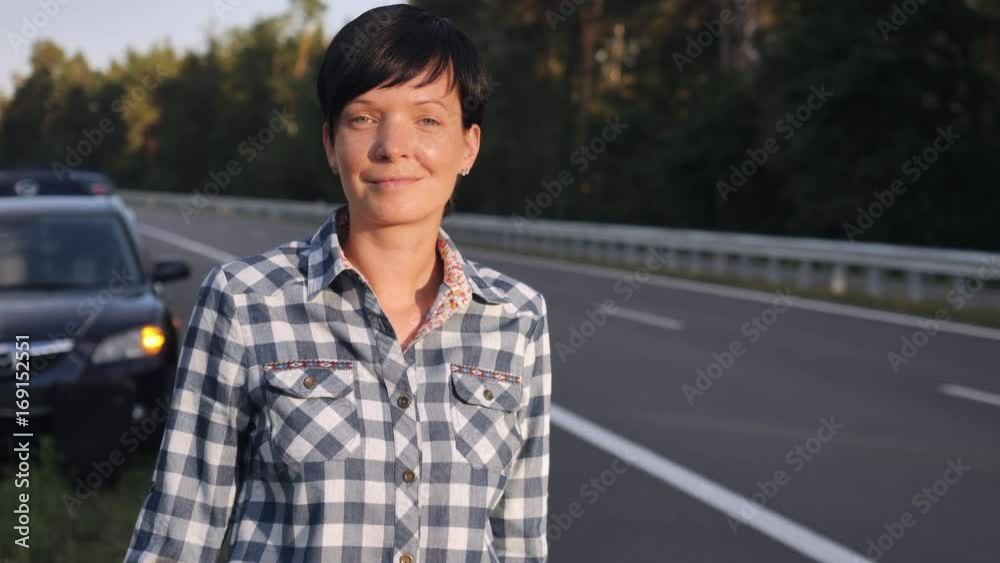 Portrait young woman standing nearby broken car the road with thumb-up try to stop car asking help. Portrait young woman standing nearby broken car the road with thumb-up try to stop car asking help.