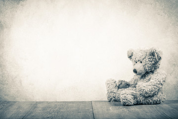 Retro Teddy Bear toy sitting alone abandoned front old textured concrete wall background. Vintage style sepia photo