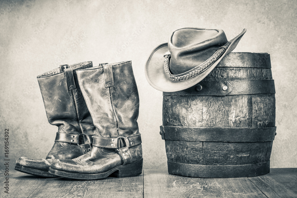 Wild West old retro leather cowboy boots, hat and oak barrel. Vintage style  sepia photo Photos | Adobe Stock