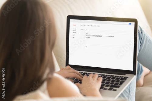 Woman typing electronic message to partner on laptop while working from home, writing commercial e-mail, composing offer in e letter, contacting client online, mail for business, close up rear view photo