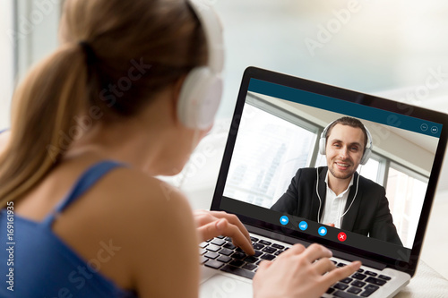 Man and woman in headphones communicating online by video call, looking at full screen videoconferencing app window, webcam videochat, virtual dating, long distance relationships, close up rear view photo