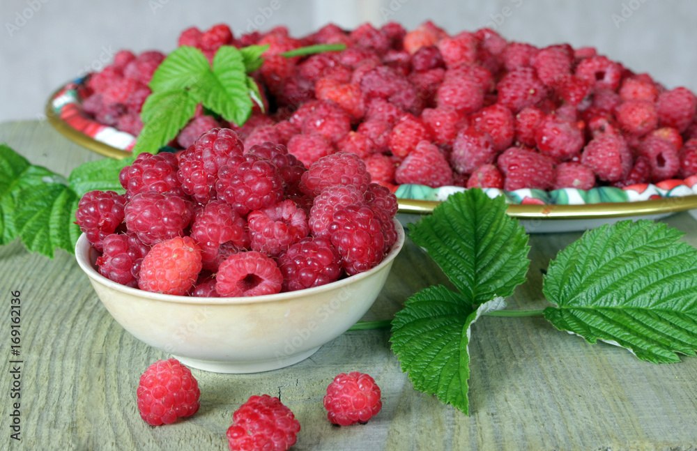 Bowl and tray natural ripe berries and green leaves on a wooden table Bowl and tray natural ripe berries and green leaves on a wooden table
