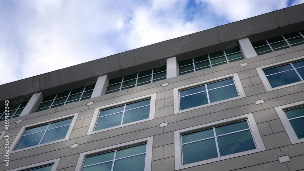 Motion of cloudy sky with illuminated reflected glass facade on modern office building Motion of cloudy sky with illuminated reflected glass facade on modern office building