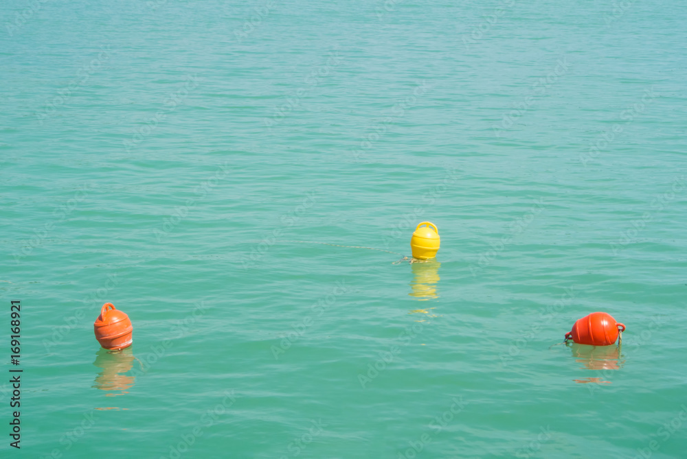 Three bright yellow and orange marker buoys floating in blue turquoise lake water, Balaton, Hungary. Abstract composition of water safety. Three bright yellow and orange marker buoys floating in blue turquoise lake water, Balaton, Hungary. Abstract composition of water safety.