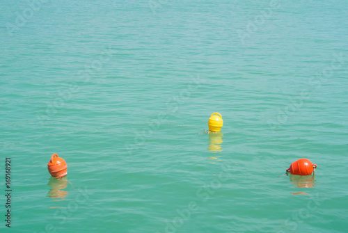 Three bright yellow and orange marker buoys floating in blue turquoise lake water, Balaton, Hungary. Abstract composition of water safety.
