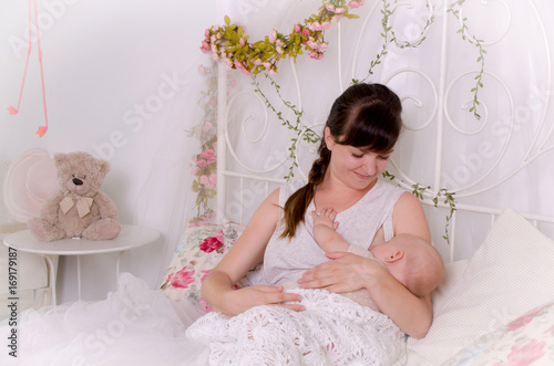Breastfeeding baby. Young mother holding her newborn child. Mom nursing baby. Woman and new born boy in white bedroom.