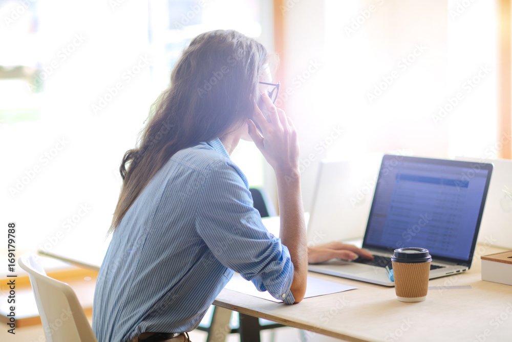 Beautiful young business woman sitting at office desk and talking on cell phone. Business woman Beautiful young business woman sitting at office desk and talking on cell phone. Business woman