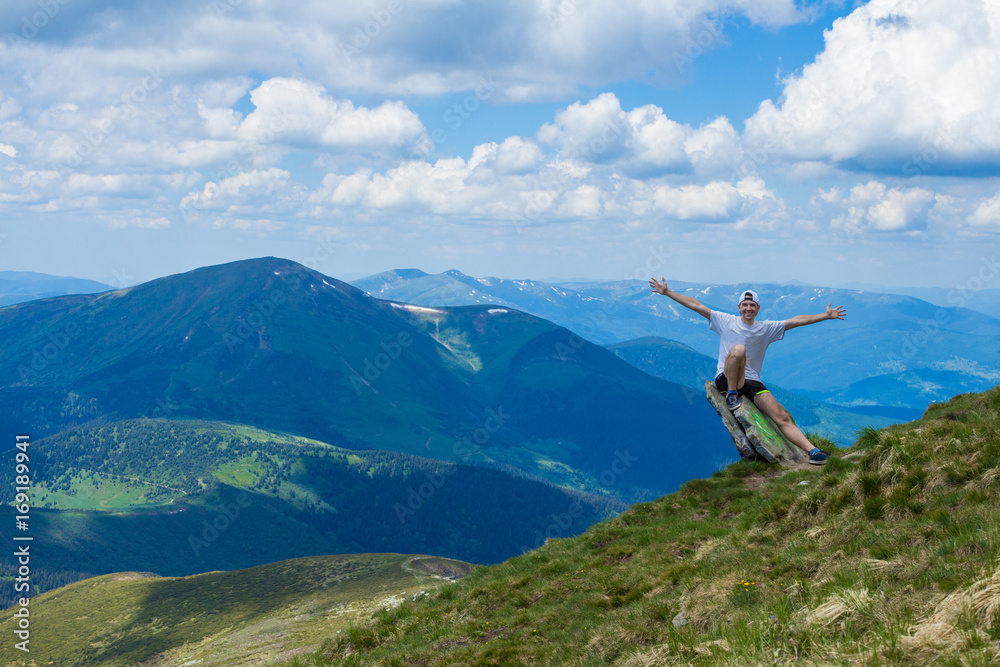 Young man tourist on cliff`s edge of mountains with hand up enjoy beautiful view of sky on top mountain. Travel and freedom concept Young man tourist on cliff`s edge of mountains with hand up enjoy beautiful view of sky on top mountain. Travel and freedom concept