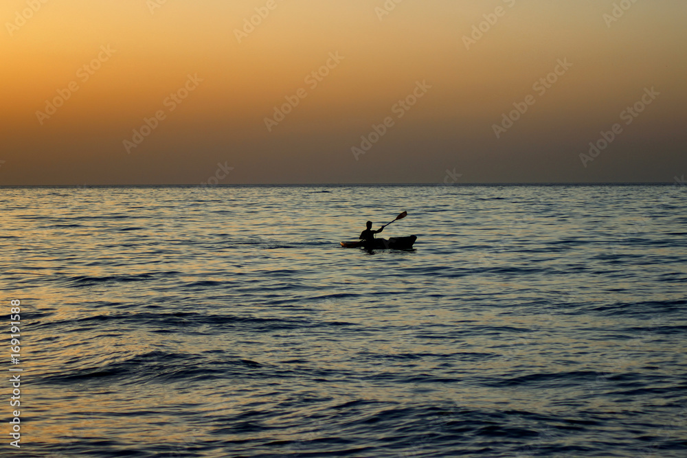 Young man floating on the canoe in the sea at sunset