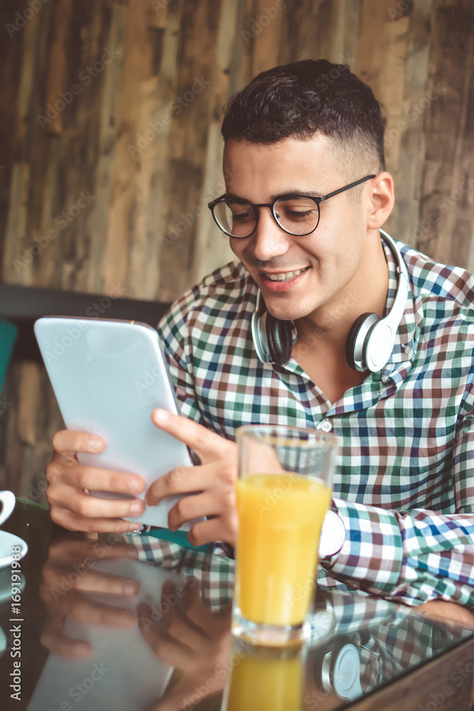 Handsome young businessman is using a tablet and smiling, sitting at bar counter in a modern urban cafe Handsome young businessman is using a tablet and smiling, sitting at bar counter in a modern urban cafe