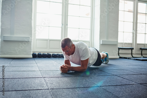 Mature man in sportswear planking on a gym floor