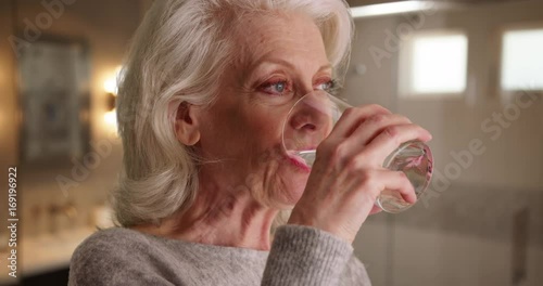Close up of attractive elder woman swallowing capsule washing it down with water. Older woman in her 50s taking pill inside bathroom to maintain health smiling. 4k 