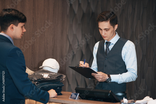 Fotografie seller in the classic clothes shop with the buyer signs the contract on the tablet