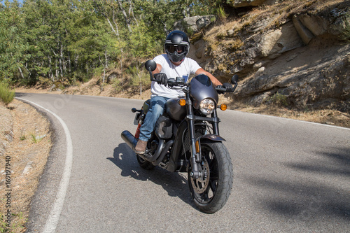 Side view of man sitting on parked custom motorcycle on road in mountains. 