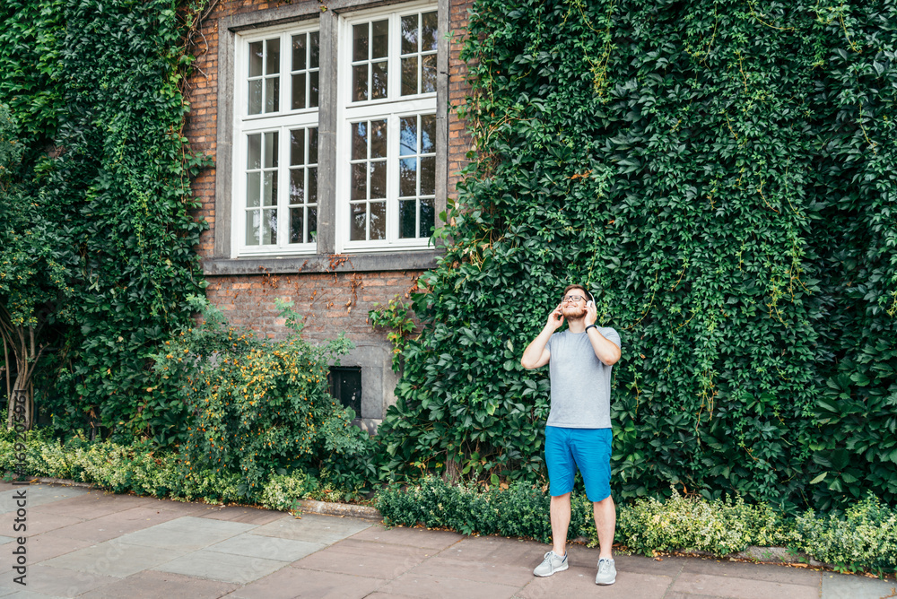 man stands in front of building in ivy and listins music man stands in front of building in ivy and listins music