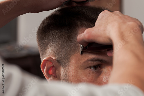 The hands of barber making haircut to young man in barbershop