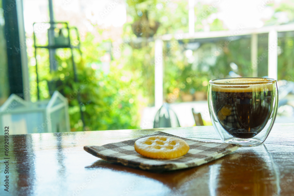 espresso coffee in transparent cup with cookies on piece of cloth on the wooden table near window.