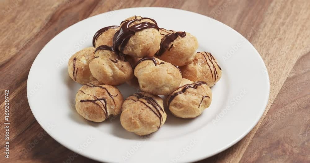 Slow motion fly out shot of profiteroles with fine dark chocolate on plate Slow motion fly out shot of profiteroles with fine dark chocolate on plate