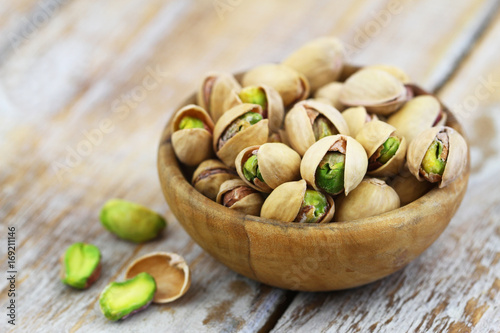 Pistachios with and without shell in bamboo bowl on rustic wooden surface
 photo