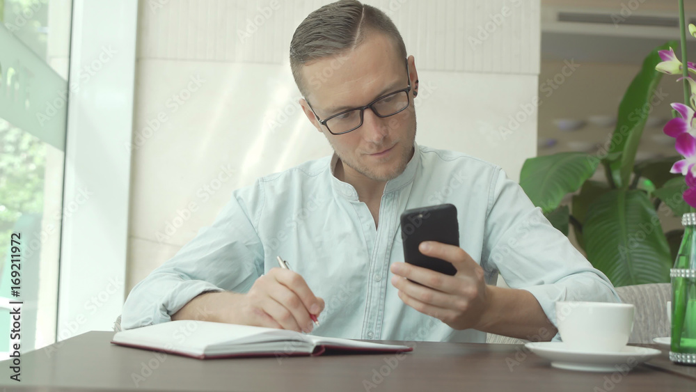 Businessman writing in daily planner and check notes on smartphone Businessman writing in daily planner and check notes on smartphone