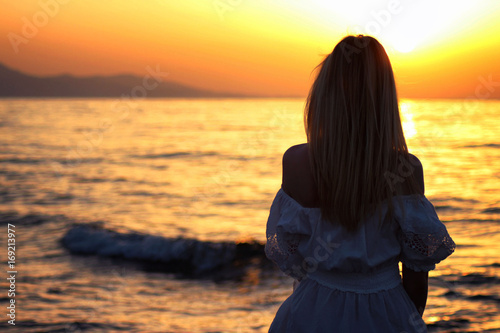 Young beautiful blonde girl sitting closeup near the sea at the sunset time