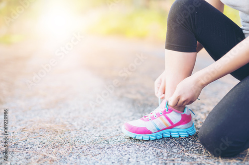 Asia woman runner jogging exercise alone to lose fat weight tying shoelaces
