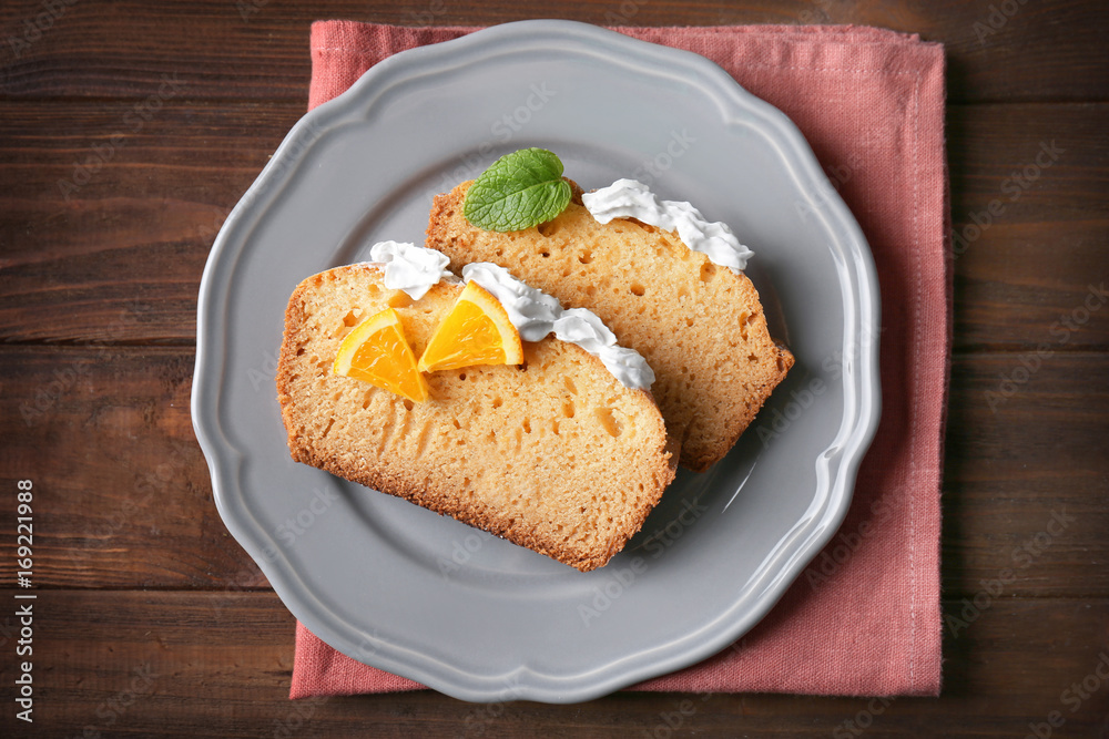 Plate with delicious sliced citrus cake with whipped cream on wooden table