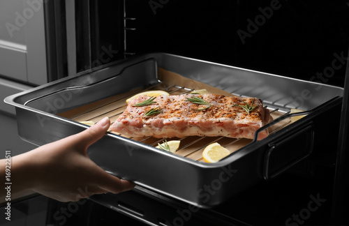 Young woman putting baking tray with pork ribs into oven