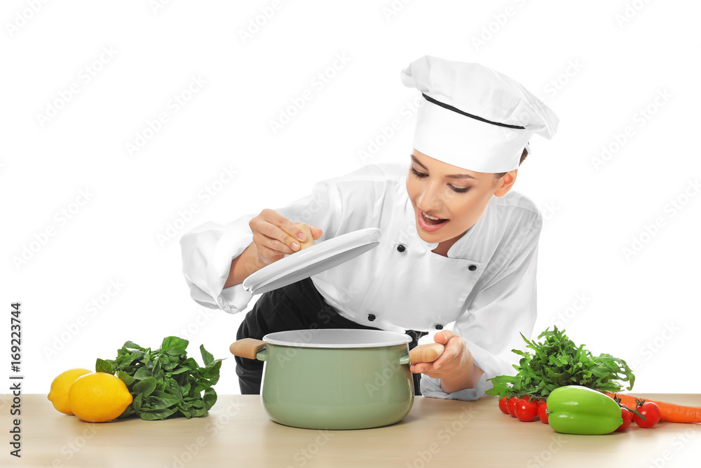 Young female chef near table with saucepan and different products, on white background Young female chef near table with saucepan and different products, on white background