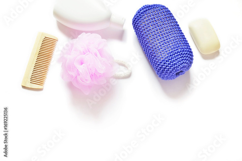 Flat lay bath products/ Shampoo bottle, wooden comb, pink and purple shower sponge, baby soap on a white background. Free space for text. Top view photo