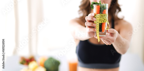 Woman holding drinking glass full of fresh fruit salad with a tape measure around the glass