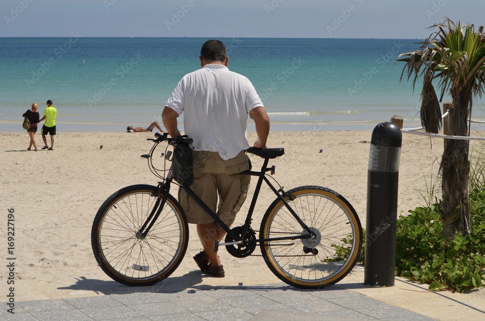 Slightly overweight man leaning on his bicycle looking out over the beach and ocean at Southpointe Park in Miami Beach,Florida.
