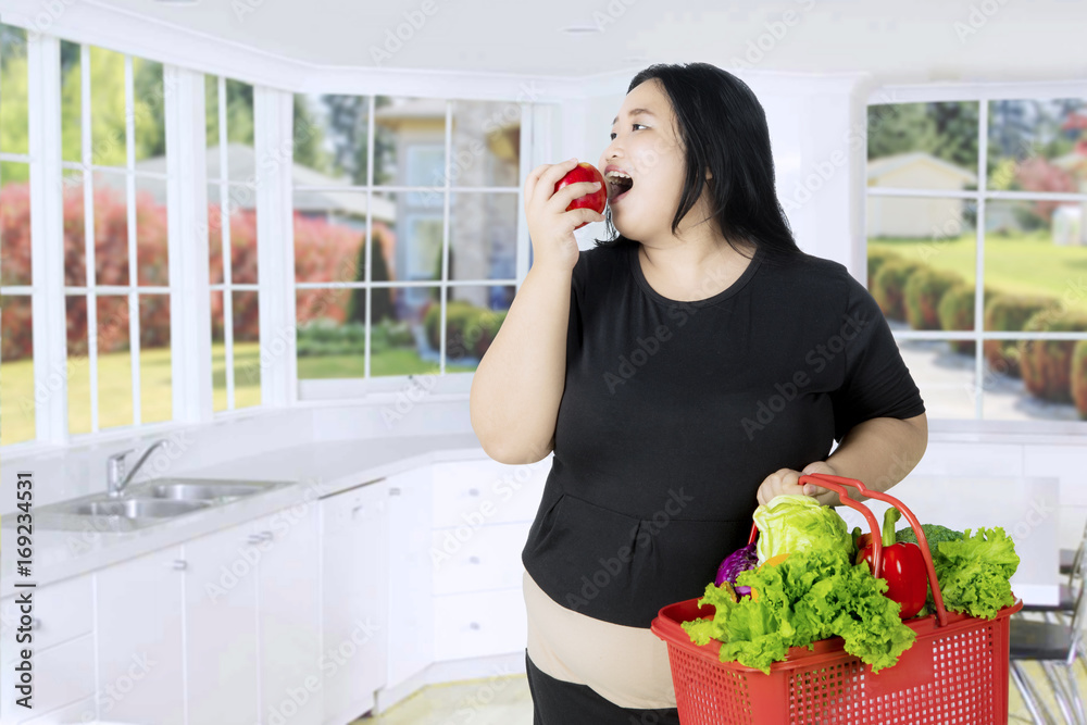 Overweight woman eating an apple in the kitchen Overweight woman eating an apple in the kitchen