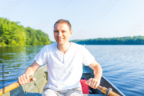 Happy smiling young man rowing boat on lake in Virginia during summer in white shirt
