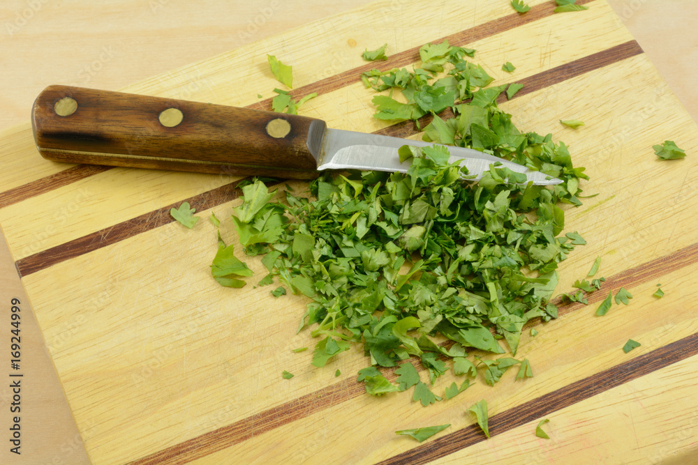 Chopping fresh cilantro on wooden cutting board with kitchen knife Chopping fresh cilantro on wooden cutting board with kitchen knife