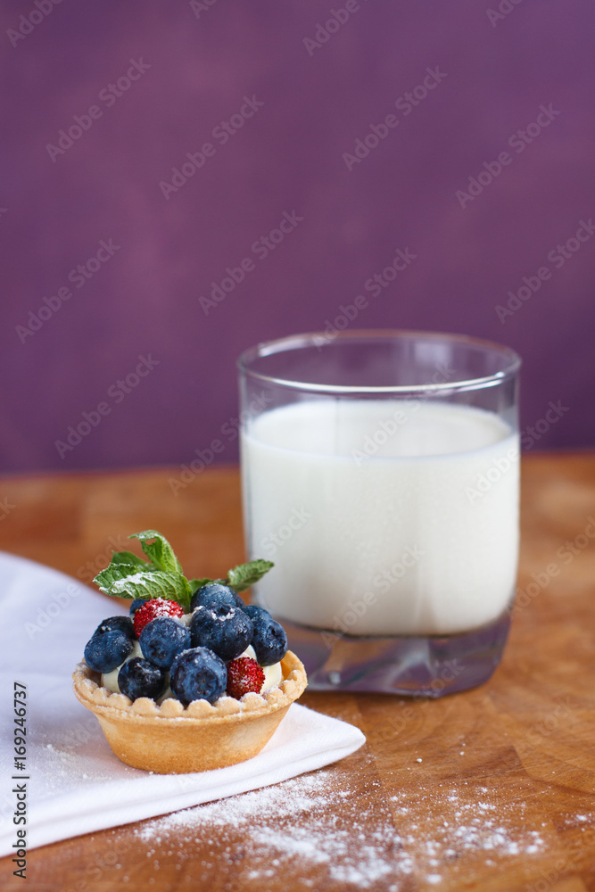 Delicious dessert blueberry tart with fresh blueberries, strawberries, mint leaves and whipped cream and a glass of milk on a wooden background Delicious dessert blueberry tart with fresh blueberries, strawberries, mint leaves and whipped cream and a glass of milk on a wooden background
