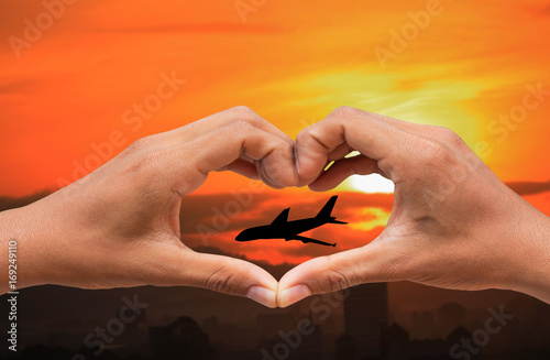 hand forming a heart shape and silhouette airplane with sunset light with copy space add text