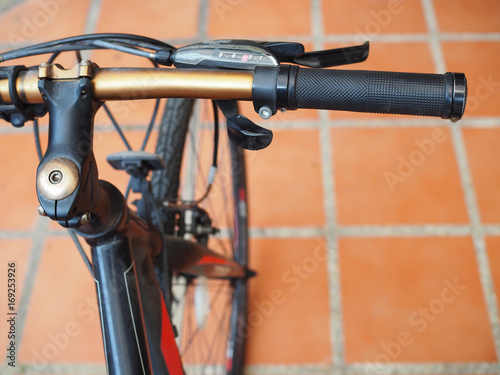 Black and golden stick hand of bicycle, with red orange clay tile floor background