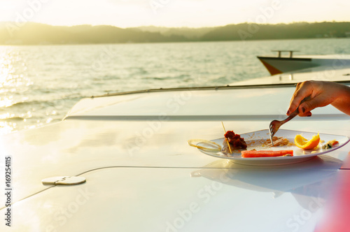 Hand with fork eating food on the deck of a yacht. A beautiful golden lens flare adds to the rich affluent theme of the shot