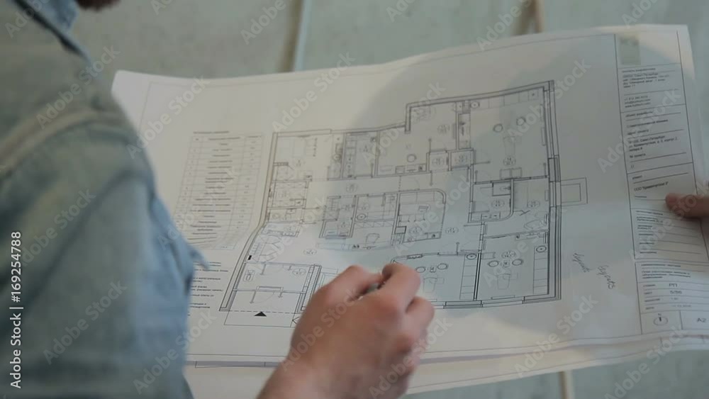 People hold hands on a sheet of drawing and show it on the handle. A large sheet is open on a large scale, with a black color depicting the layout of the apartment in the house. Foreman discusses the