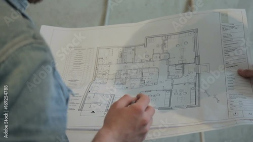 People hold hands on a sheet of drawing and show it on the handle. A large sheet is open on a large scale, with a black color depicting the layout of the apartment in the house. Foreman discusses the