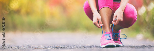 Running shoes runner woman tying laces for autumn run in forest park panoramic banner copy space. Jogging girl exercise motivation heatlh and fitness.