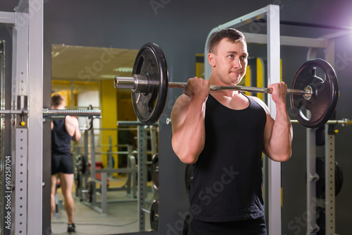 Strong and handsome man lifting weights a barbell in a gym